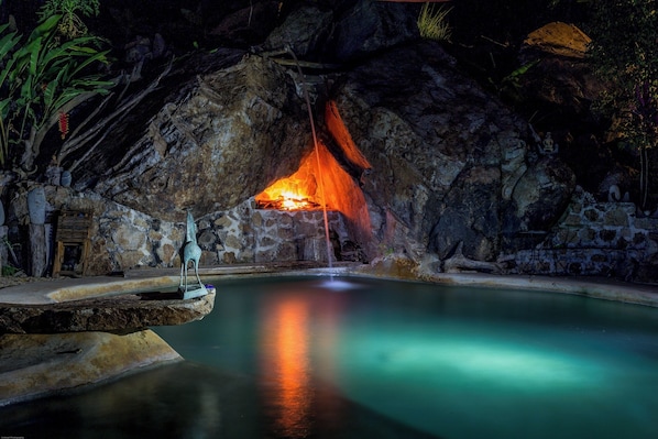 Une grotte avec un foyer, une piscine et des statues.