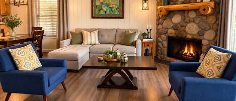 A cozy living room with a fireplace, blue sofas, a wooden coffee table, and a stone wall.