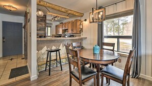 Una cocina con armarios de madera, un comedor con una mesa redonda y sillas, y un ventanal con vistas a árboles.