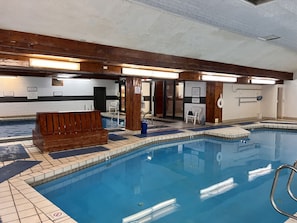 An indoor swimming pool with a wooden bench, tiled flooring, and a clear blue pool.