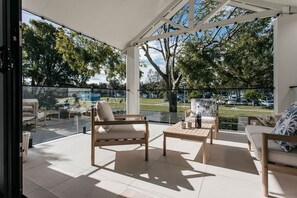 A covered outdoor seating area with wooden furniture and a glass barrier. - Clarkes Beach Elevated. Water front. Ocean views from cozy sun drenched balcony. (Byron Bay)