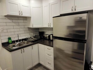 A kitchen with white cabinets, a stainless steel refrigerator, a sink, and a coffee maker.
