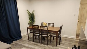 Un comedor con mesa y sillas de madera, una planta en maceta y una cortina azul.