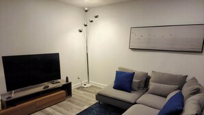 Una sala de estar moderna con un televisor de pantalla plana, un sofá con cojines azules, una lámpara de pie y un cuadro en la pared.