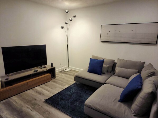 A modern living room with a flat-screen TV, a sofa with blue cushions, a floor lamp, and a painting on the wall.