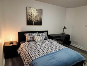 Une chambre à coucher comprenant un lit, un bureau, une chaise, une table de chevet, une lampe et un tableau accroché au mur.