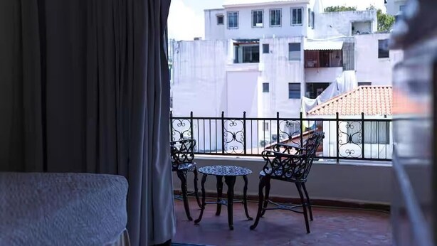 A balcony with a table and chairs, a view of buildings, and a curtain. - Spacious Central w/ Balcony + Kitchen - 2 Beds (Santo Domingo)
