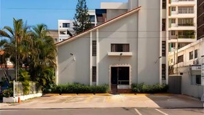 A modern building with a flat roof, a central entrance, and a parking lot in front. - Spacious Central w/ Balcony + Kitchen - 2 Beds (Santo Domingo)