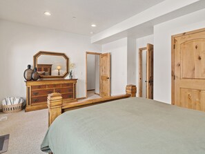 A bedroom with a bed, dresser, mirror, and wooden doors.