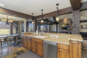 A kitchen with a large island, wooden cabinets, a dishwasher, and a stone fireplace. - Edgewater Getaway EW103 |Lakefront |Hot Tub |Pool (Huntsville)