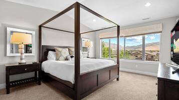 A four-poster bed with a dark finish, a bedside table with a lamp, and a large window offering a view of a mountainous landscape.