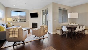 A modern living room with a fireplace, a dining area with a table and chairs, and a large window with a view. - Shred Reckoning | Pineview | Pool |  Hot Tub (Huntsville)