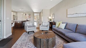 A modern living room with a round coffee table, two armchairs, a sofa, and a dining area in the background. - Shred Reckoning | Pineview | Pool |  Hot Tub (Huntsville)