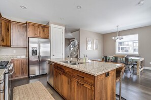 Una cocina con armarios de madera, un refrigerador de acero inoxidable, una encimera de granito y un comedor con mesa y sillas.