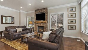 A living room with a stone fireplace, leather sofas, a coffee table, and framed pictures on the wall. - Lakeside Getaway LS14A | Hot Tub | Dog-Friendly (Huntsville)