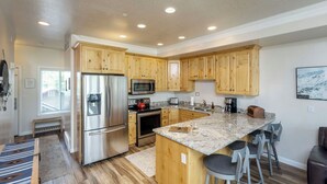 A modern kitchen with wooden cabinets, stainless steel appliances, granite countertops, and bar stools. - Lakeside Cove Retreat LS18|Hot Tub |Pool |Pineview (Huntsville)
