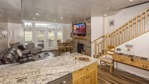 A kitchen with a granite countertop, a stone fireplace, a wooden dining area, and a staircase. - Lakeside Cove Retreat LS18|Hot Tub |Pool |Pineview (Huntsville)