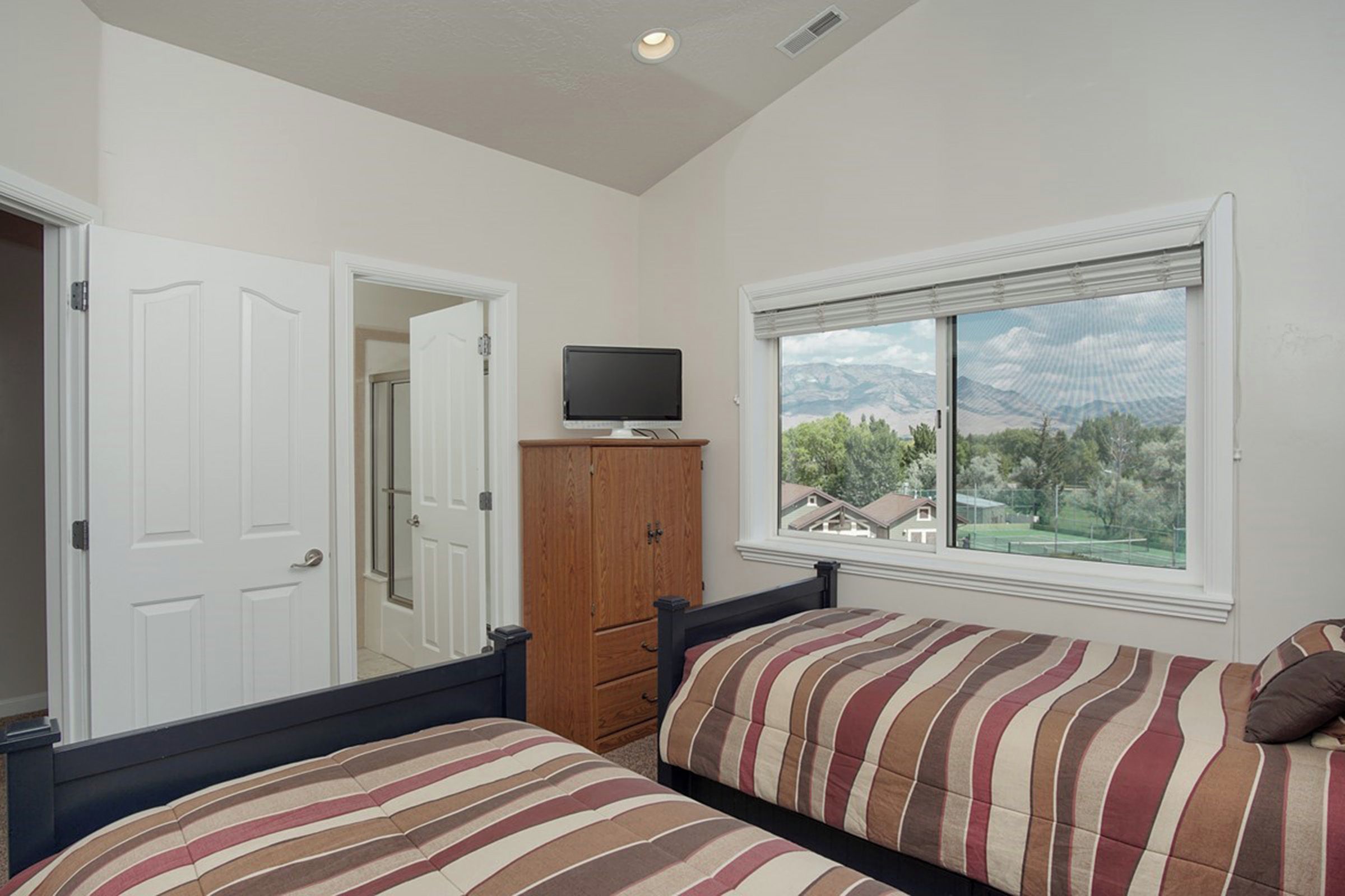 Un dormitorio con dos camas, un televisor sobre un mueble, un armario y una ventana con vistas.