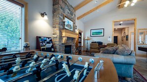 A cozy living room with a foosball table, a stone fireplace, and a comfortable sofa. - Lakeside Cove Retreat LS18|Hot Tub |Pool |Pineview (Huntsville)