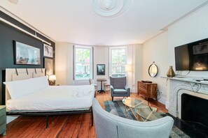 A hotel room with a bed, a TV, a fireplace, and a window with a view of greenery. - Beacon Hill Charm - Prime Boston Stay (Boston)