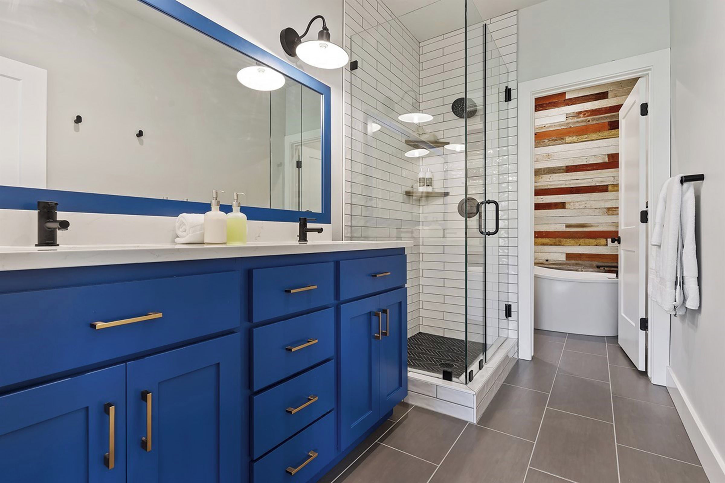 Un bagno moderno con un mobile lavabo blu, uno specchio grande, uno sportello doccia in vetro e una vasca da bagno bianca.