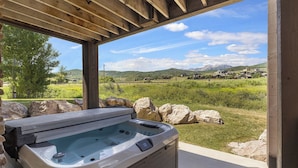 Un bain à remous sous une pergola en bois, avec vue sur un paysage verdoyant et des montagnes.