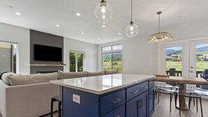 Une cuisine moderne dotée d’un îlot central, de meubles bleus et d’un coin repas avec une grande table et des chaises.