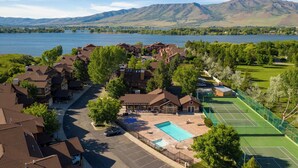 Un quartier résidentiel avec des maisons, une piscine, des courts de tennis et un lac, avec des montagnes en toile de fond.