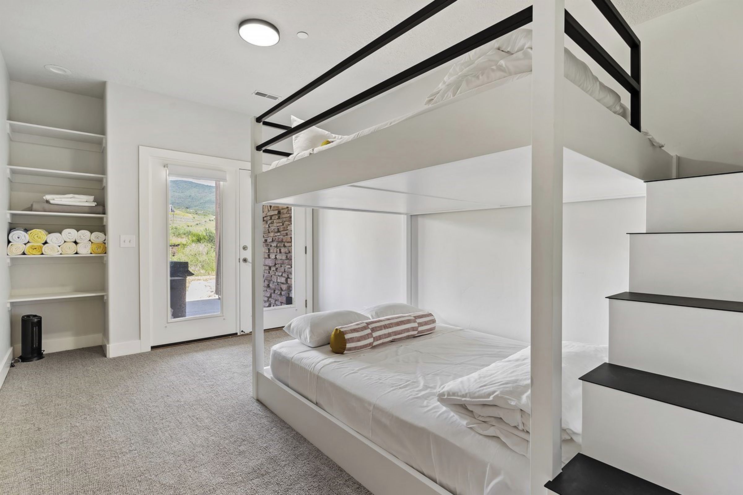 Een slaapkamer met stapelbedden, een wit kleurenschema, een deur naar een buitengebied en een plank met handdoeken.