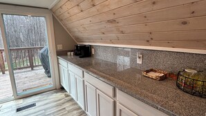 Eine Küche mit Holzboden, Granitarbeitsplatte, weißen Schränken und Blick auf eine Terrasse.