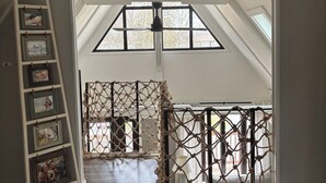 Ein Zimmer mit schrägen Wänden, einer Holzleiter, einem Seilnetz und gerahmten Bildern an der Wand.