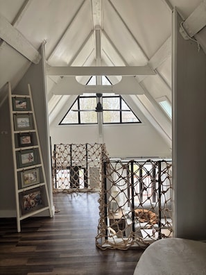 Ein Zimmer mit schrägen Wänden, einer Holzleiter, einem Seilnetz und gerahmten Bildern an der Wand.