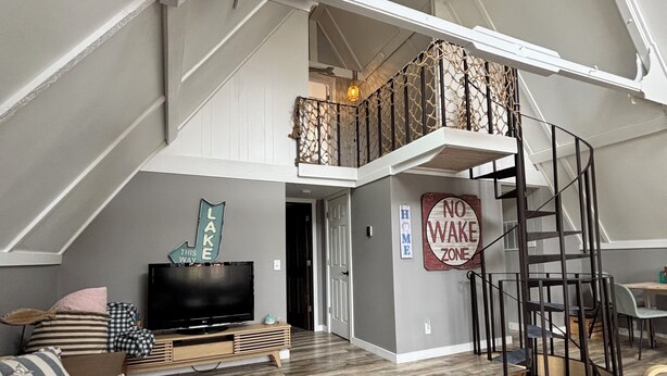 Ein geräumiges Loft mit hoher Decke, einer Treppe, einem Fernseher und einem Schild mit der Aufschrift 'No Wake Zone'.