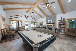 Een pooltafel in een ruimte met houten balken, een open haard en een boekenkast.