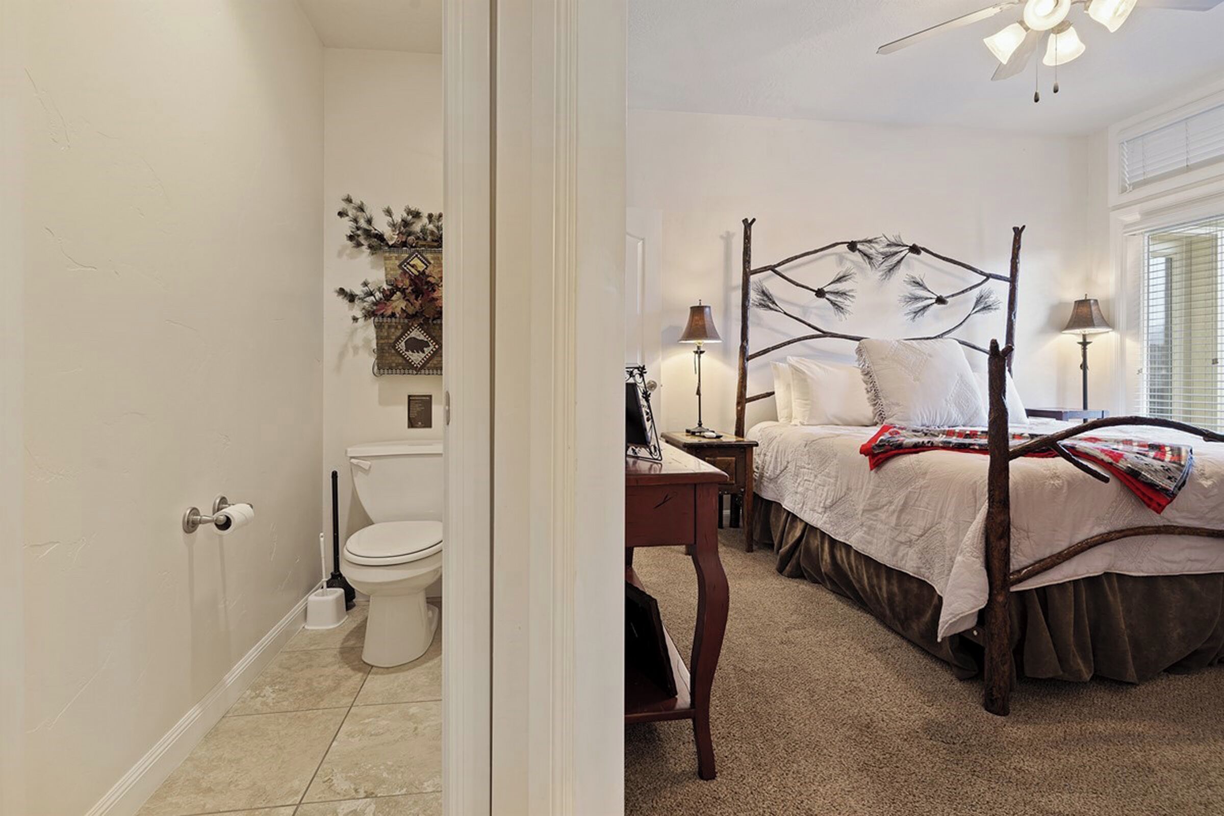 A bedroom with a four-poster bed, a bedside table, a lamp, and a view of the bathroom.