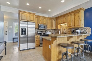 A modern kitchen with wooden cabinets, stainless steel appliances, a granite countertop, and a bar area with stools. - Westhaven Retreat LS31 |Hot tub | Pool |Pickleball (Huntsville)