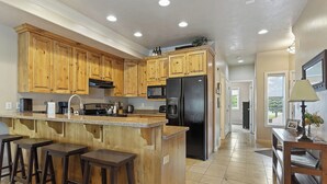 Una cocina con armarios de madera, un refrigerador negro, un microondas y una zona de bar con taburetes.