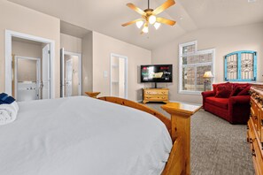 A hotel room with a large bed, a wooden headboard, a television, a red sofa, and a window with a decorative screen. - Paddle & Ski Retreat LS43 |Hot Tub |Pineview |Pool (Huntsville)