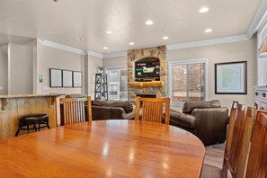 A dining area with a wooden table, brown leather couches, and a stone fireplace with a TV displaying streaming services. - Paddle & Ski Retreat LS43 |Hot Tub |Pineview |Pool (Huntsville)