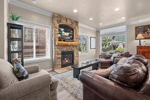 A living room with a stone fireplace, leather sofas, a coffee table, and a TV mounted on the wall. - Paddle & Ski Retreat LS43 |Hot Tub |Pineview |Pool (Huntsville)