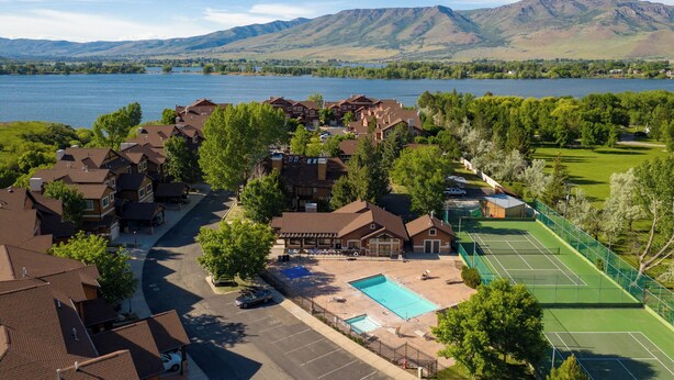 Un quartiere residenziale con case, una piscina, campi da tennis e un lago sullo sfondo di montagne.