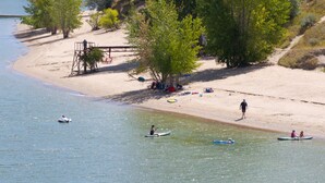 Una spiaggia con persone che pagaiiano in canoe, una torretta di salvataggio e una riva sabbiosa con alberi.