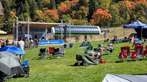 Un’area verde con tende, sedie, un palco e un edificio con un cartello che riporta la scritta “Summer at Snowbasin”.