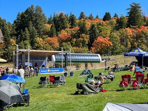 A grassy area with tents and chairs, a stage, and a building with a sign that reads "Summer at Snowbasin". - Paddle & Ski Retreat LS43 |Hot Tub |Pineview |Pool (Huntsville)