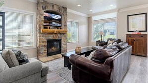 A living room with a stone fireplace, leather sofa, and a television mounted on the fireplace. - Paddle & Ski Retreat LS43A |Pool |Hot Tub|Pineview (Huntsville)