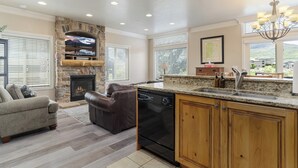 A spacious kitchen with a stone fireplace, a built-in dishwasher, and a large island with a sink. - Paddle & Ski Retreat LS43A |Pool |Hot Tub|Pineview (Huntsville)