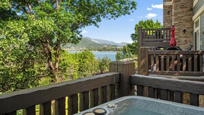 Ein Whirlpool mit einer Holzdar Terrasse, ein Steinhaus und Blick auf einen See und Berge.