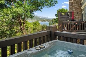 A hot tub with a wooden deck, a stone building, and a view of a lake and mountains. - Pineview Lakeside Retreat LS45 | Hot Tub | Pool (Huntsville)