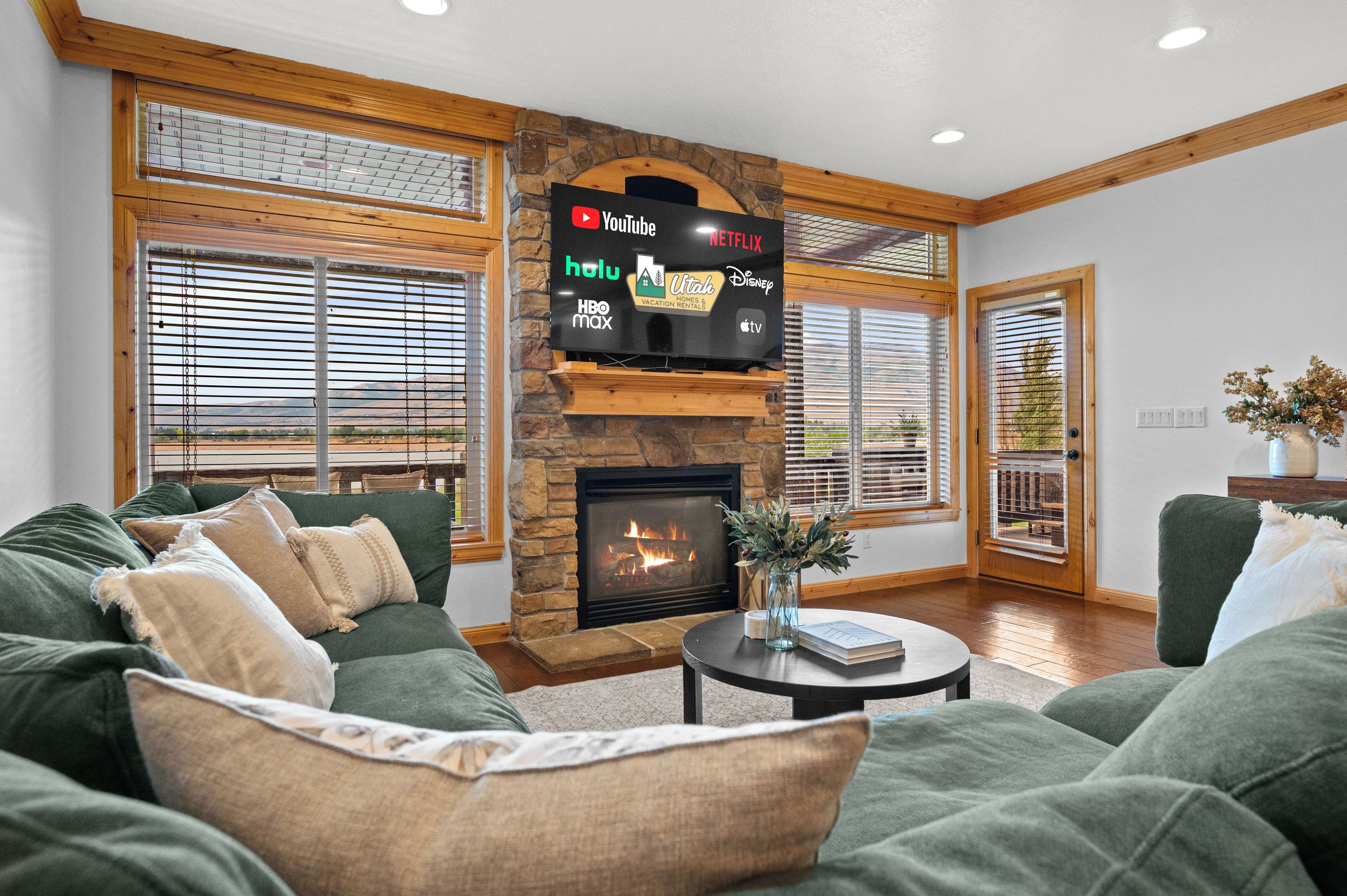 Una sala de estar con chimenea de piedra, un televisor de pantalla plana grande montado encima y un conjunto de sofá verde.