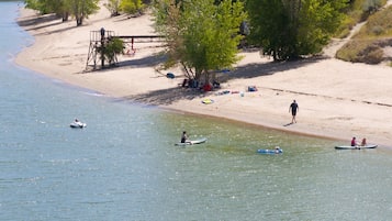 A beach with people paddling in canoes, a lifeguard tower, and a sandy shore with trees.